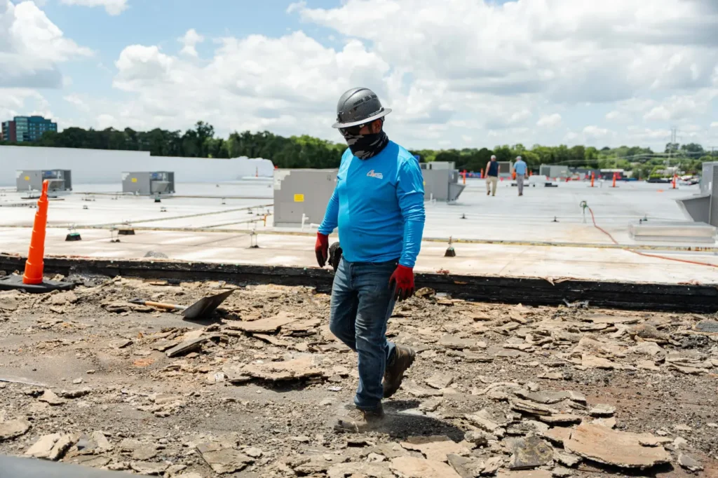 Cox Bros Roofing worker in safety gear walking across a commercial flat roof during a roof repair or replacement project.