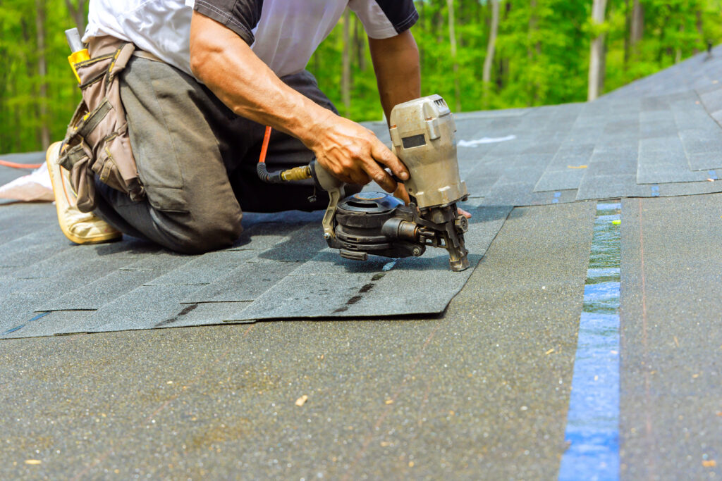 Roofer worker installing new bitumen shingles on roof used an air pneumatic nail gun.